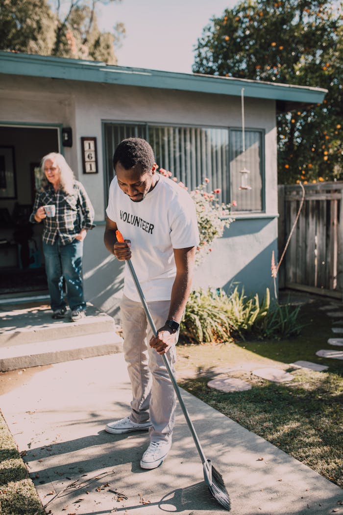 Young volunteer sweeping outdoor yard during a community service event on a sunny day.